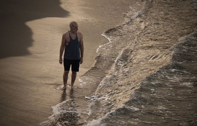 Full length of man walking on beach with ocean wave during sunrise