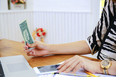 Midsection of woman using mobile phone while sitting on table