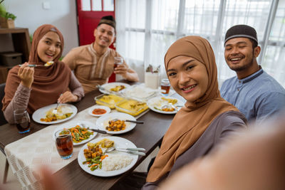 Smiling woman taking selfie while sitting at dining table