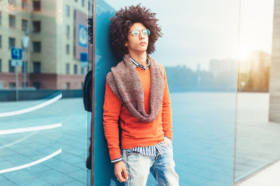 Young man with curly hair standing against wall