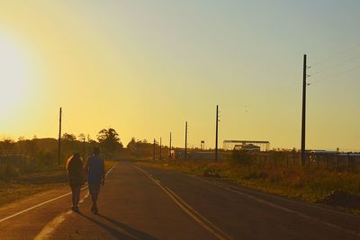 Men on road against sky during sunset