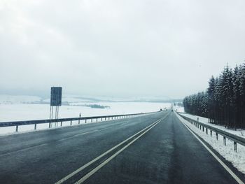 Road by trees against sky during winter