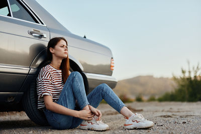 Portrait of young woman sitting on car