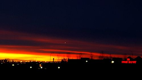 Illuminated city against sky at sunset
