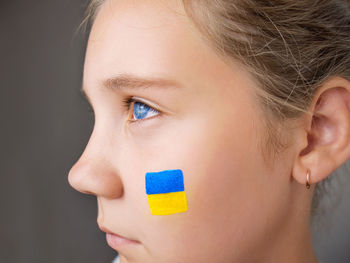 Portrait of a sad girl with blue eyes with the flag of ukraine on her cheek, close-up
