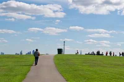 Rear view of people walking on field against cloudy sky