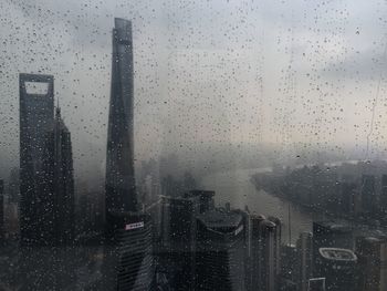 Buildings in city seen through wet window during rainy season