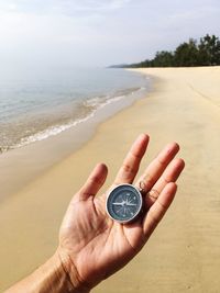 Cropped hand holding navigational compass at beach on sunny day