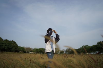 Rear view of woman standing on field against sky