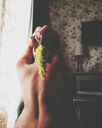 Rear view of topless woman holding grapes at home