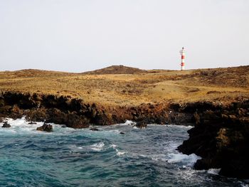 Lighthouse by sea against clear sky