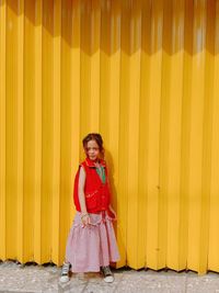 Portrait of a smiling girl standing against yellow wall