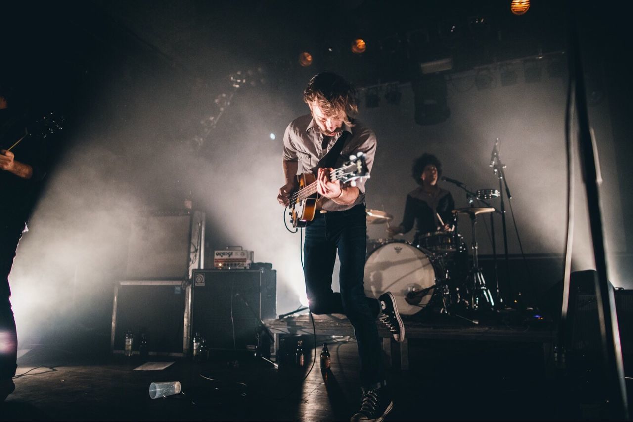 MAN PLAYING GUITAR AT ILLUMINATED STAGE