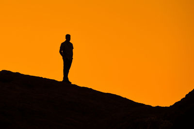 Silhouette man standing on field against clear orange sky