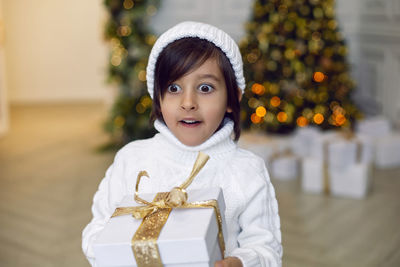 Boy in a white knitted sweater and hat stands with gift box 