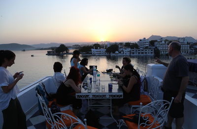 People sitting on table by sea against sky during sunset