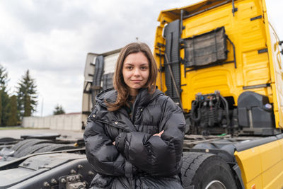 Portrait of young woman standing against car