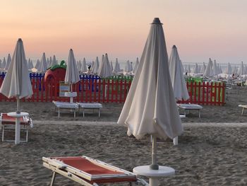 Lounge chairs and tables on beach against sky during sunset