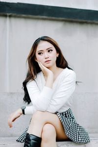 Portrait of young woman sitting against wall