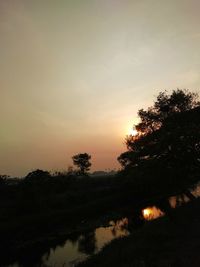 Silhouette trees by lake against sky during sunset