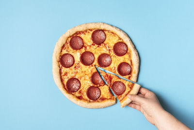 Close-up of hand holding pizza over white background