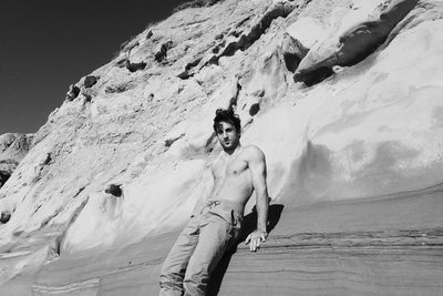 Low angle view of shirtless man standing by rock formation