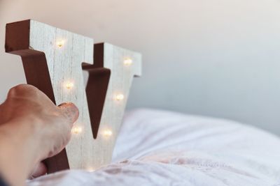 Cropped hand holding illuminated wooden v shape on bed