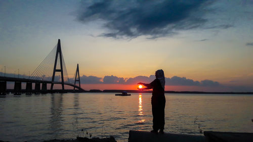 Silhouette bridge over bay against sky during sunset