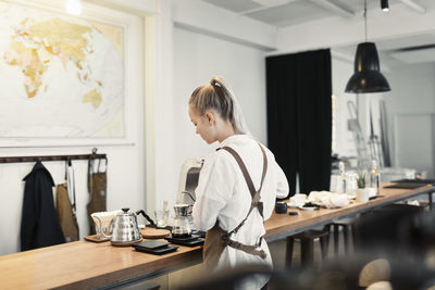 Rear view of young female barista preparing coffee at counter