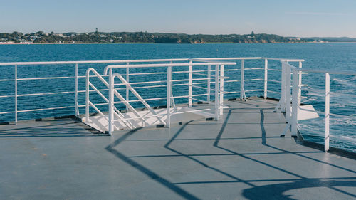 Chairs by swimming pool against sea against clear sky