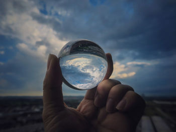 Cropped hand of person holding crystal ball against sky