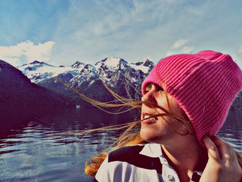 Woman wearing knit hat against lake in sunny day