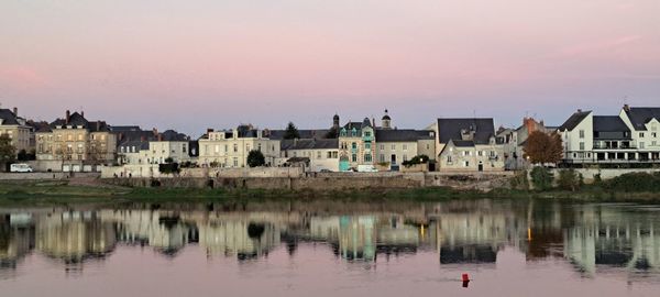 Buildings by lake against sky during sunset