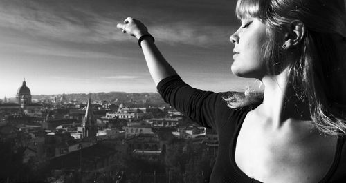 Young woman standing with arms outstretched against cityscape