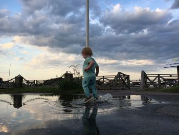 Boy jumping in puddle against sky during sunset