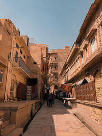 People walking amidst buildings in city against clear sky