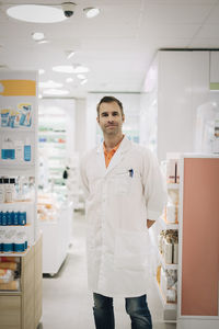 Portrait of confident mature male pharmacist standing at medical store