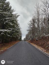 Empty road amidst trees against sky