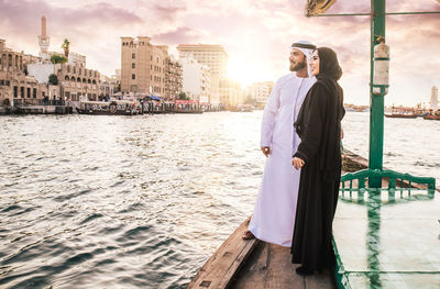 Smiling couple looking at view while standing in boat on river during sunset