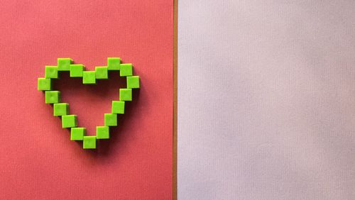 High angle view of green toy blocks in heart shape on red paper