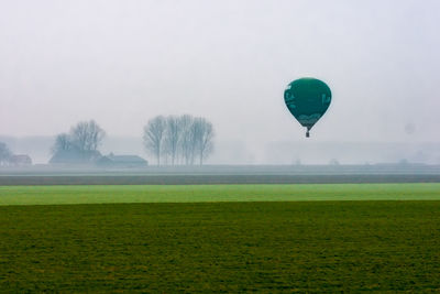 Hot air balloon flying over field against clear sky