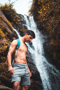 Travel and freedom. young shirtless boy in shorts with rucksack enjoying tropical waterfall view.