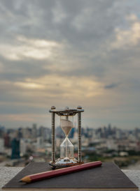 Close-up of clock on table in city against sky