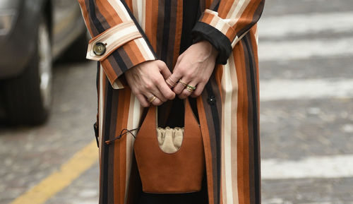 Midsection of woman holding purse while standing on road