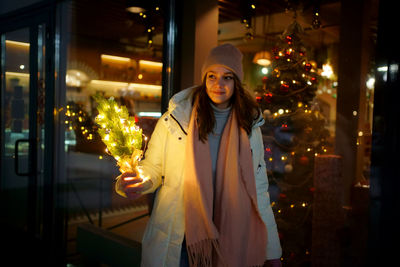 Caucasian white girl near a shop window, with a christmas tree in her hands, christmas shopping