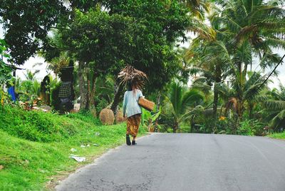 Rear view of woman transporting bundle of palm leaves on her head