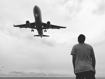 Rear view of man looking at airplane flying in sky