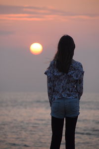 Rear view of woman standing on beach during sunset