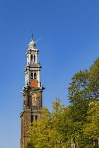 Low angle view of bell tower by tree against blue sky