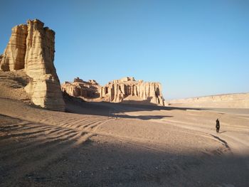 Man standing on rock formation in desert against clear sky